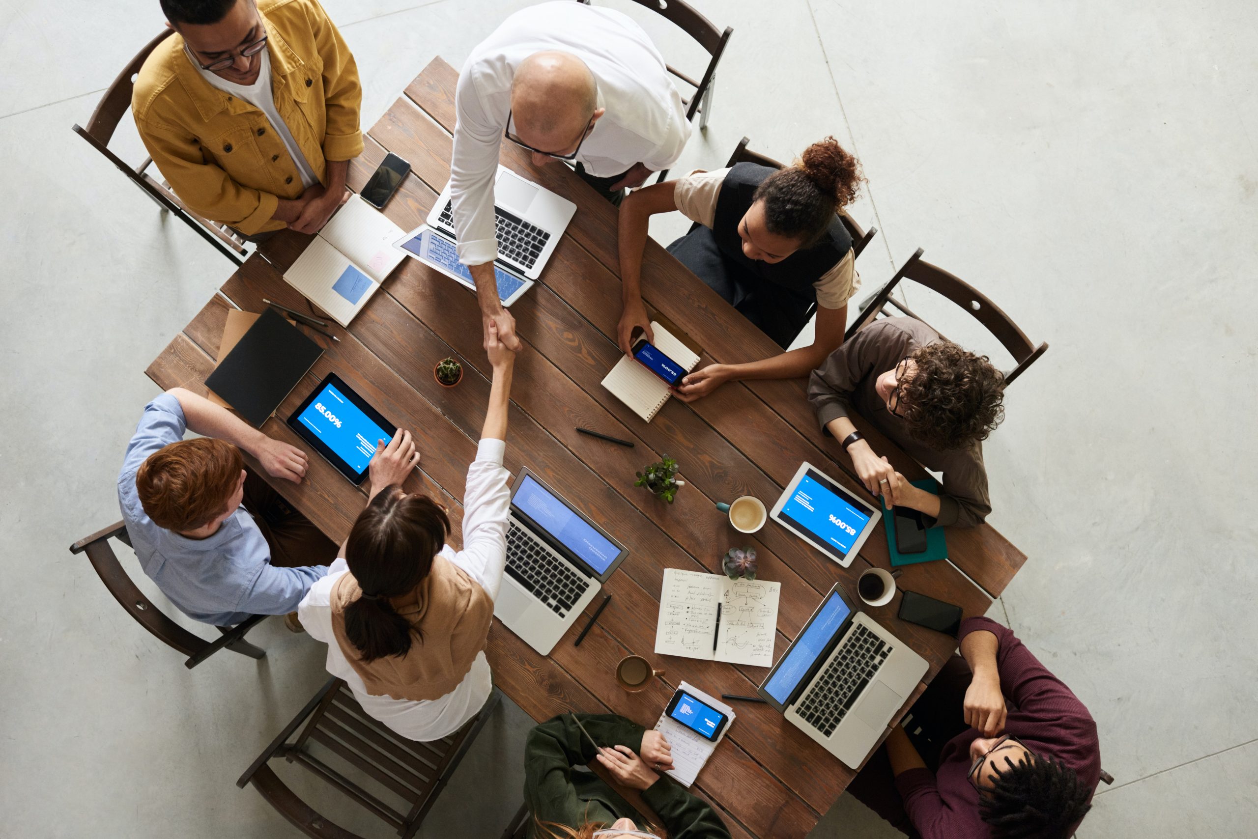 Group of eight people sitting around a table working and talking with laptops. Image is looking down on them from above.