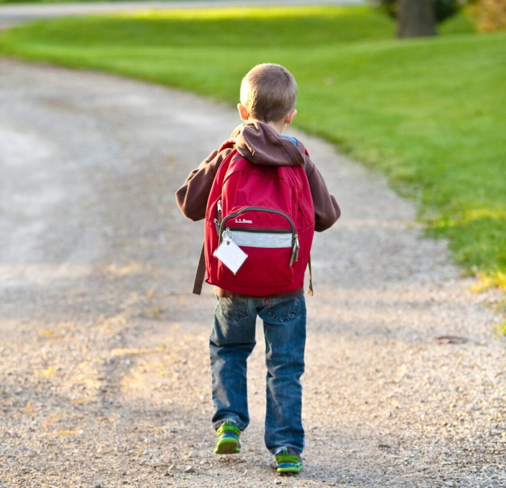 A young boy walks on a path carrying a red backpack